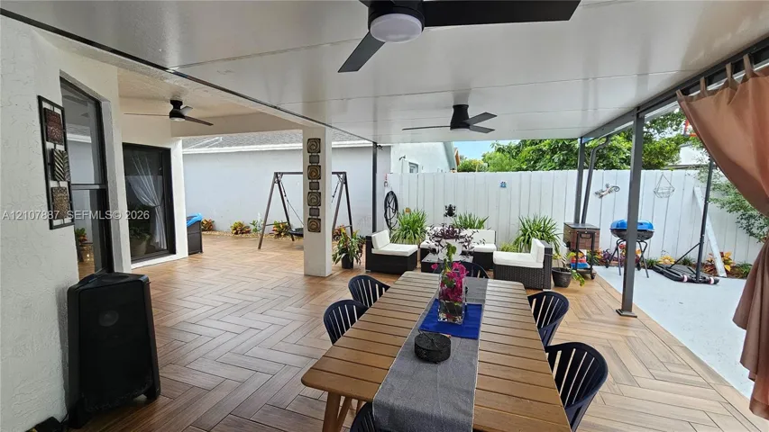 Covered patio featuring herringbone-patterned tile flooring, multiple ceiling-mounted fans, and white privacy fencing