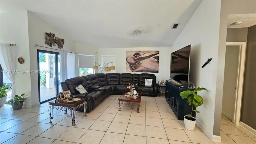 Living area featuring vaulted ceilings, neutral ceramic tile flooring, and sliding glass doors providing outdoor access