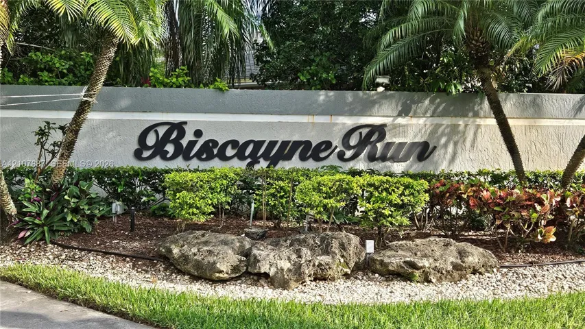 Biscayne Run monument signage featuring a textured masonry wall, dimensional lettering, decorative boulder accents, and professional tropical landscaping
