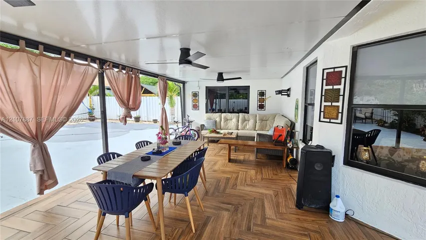 Covered patio featuring wood-finish flooring in a herringbone pattern, integrated ceiling fans, and large windows