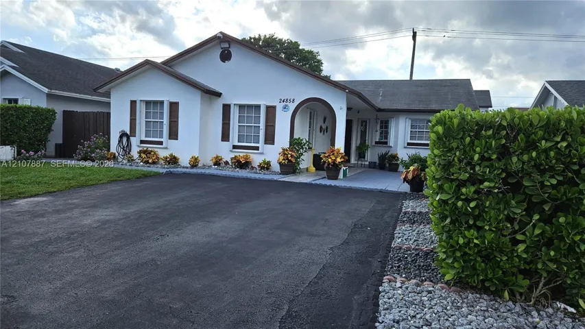 Single-story exterior featuring a light-toned stucco façade, an arched entryway, shingle roof, and decorative window shutters
