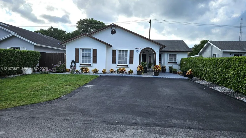 Stucco exterior featuring decorative window shutters, an arched entryway, a paved driveway, and established perimeter hedging