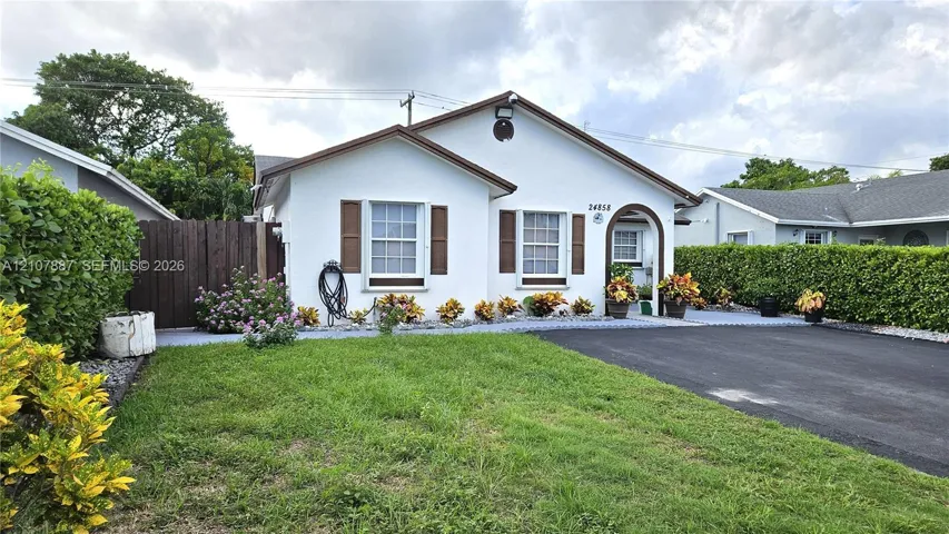 Single-story exterior featuring white stucco finish, decorative and accordion shutters, an arched entry, and a paved driveway