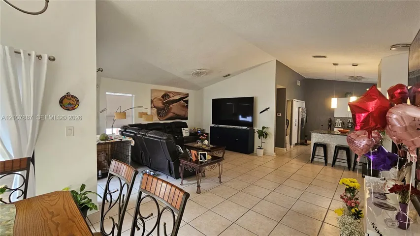 Open-concept interior featuring vaulted ceilings, neutral tile flooring, recessed lighting, and a kitchen island with stone-finish countertops