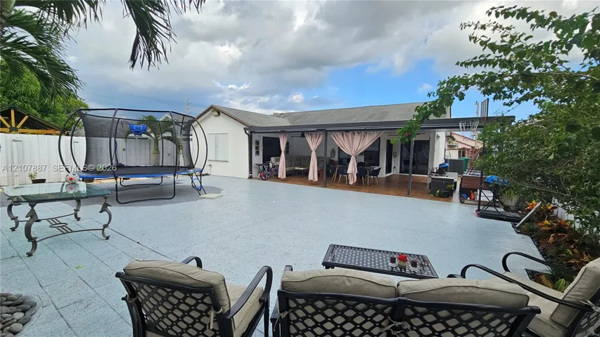 Spacious backyard featuring an expansive paved patio, a covered lanai, and white privacy fencing