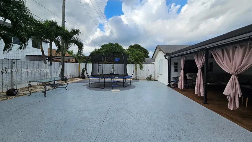 Expansive outdoor patio with concrete surfacing, covered rear porch featuring wood-finish flooring, and white vinyl perimeter fencing