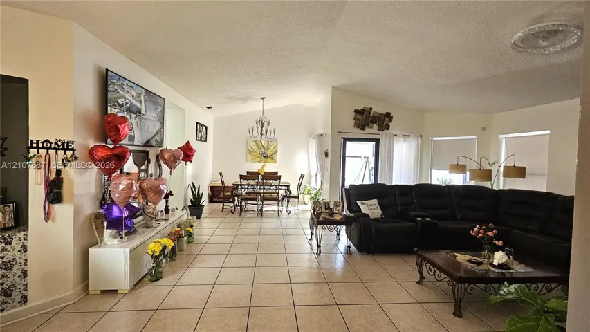 Open-concept floor plan featuring vaulted ceilings, neutral ceramic tile flooring, and a decorative tiered chandelier
