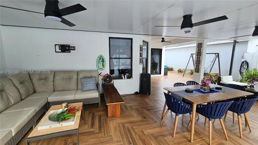 Covered patio featuring wood-finish flooring laid in a herringbone pattern, three mounted ceiling fans, and high-contrast window trim