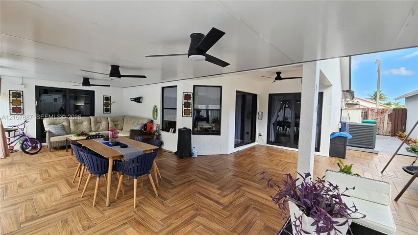 Covered patio featuring wood-finish flooring in a herringbone pattern, multiple ceiling fans, and dark-framed window and door casings