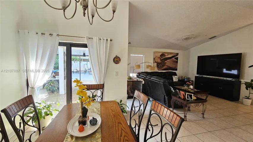 Vaulted ceilings, ceramic tile flooring, multi-arm chandelier, and sliding glass door leading to a screened lanai