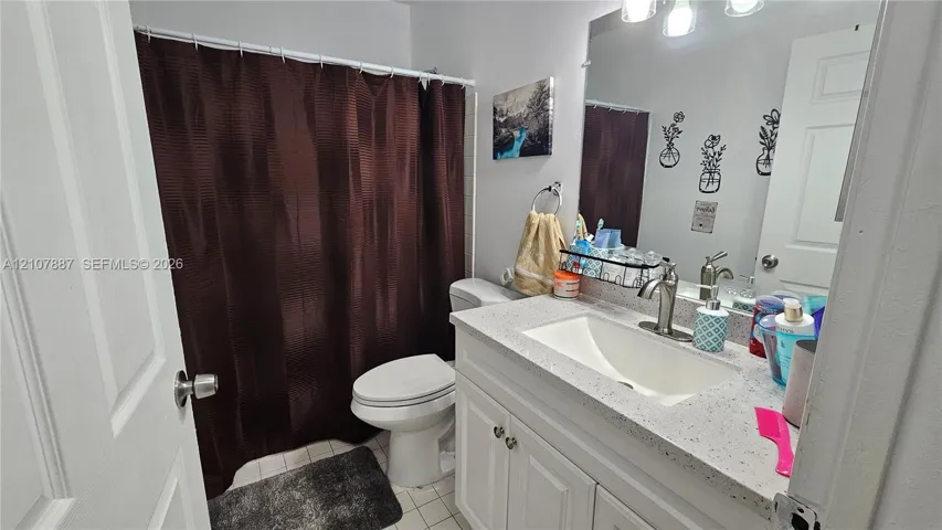Bathroom featuring a white vanity cabinet, light-colored stone-finish countertop with an integrated basin, high-arc brushed nickel faucet, large wall-mounted mirror, and three-light fixture