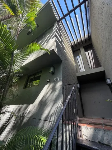 Stucco exterior featuring a wood-slat pergola, metal railing, recessed wall-mounted lighting, and tile-surfaced entry stairs