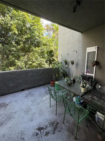 Covered balcony featuring textured concrete flooring, stucco wall finish, and mature tree canopy
