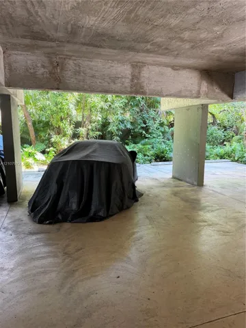 Covered parking area featuring concrete pillars, a textured concrete ceiling, and a concrete floor