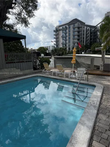 In-ground swimming pool with built-in stairs, concrete paver decking, and a private wooden dock situated on a waterway