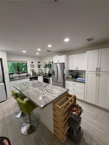 Kitchen featuring a stone-topped central island, recessed ceiling lighting, white cabinetry, stainless steel appliances, and wood-finish flooring