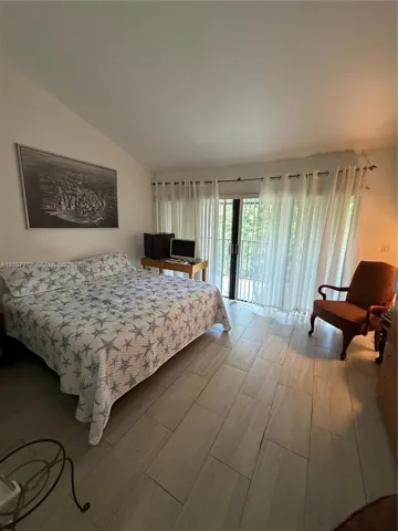 Room featuring a vaulted ceiling, wood-finish tile flooring, and glass sliding doors providing access to an exterior balcony