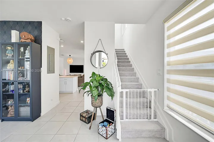 Entryway featuring large-format tile flooring, a geometric patterned accent wall, recessed lighting, and a staircase with neutral carpeting and a white handrail