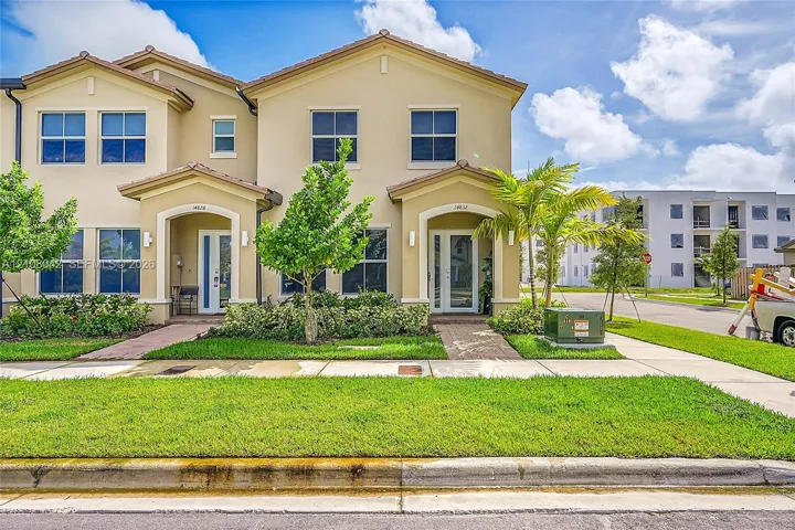 Two-story stucco exterior featuring a hipped roof, covered entryways with arched detailing, glass-panel front doors, and concrete walkways