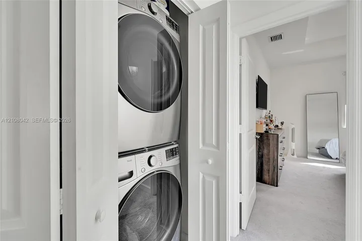 Laundry closet featuring a stacked front-loading washer and dryer set with metallic finish and bifold doors