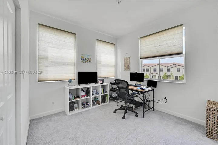 Neutral interior room featuring wall-to-wall carpeting, three multi-pane windows, and neutral roller shades
