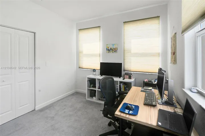 Interior room featuring neutral wall-to-wall carpeting, dual-panel closet doors, and three windows fitted with light-filtering cellular shades