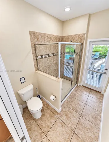 Enclosed glass-door shower featuring tile surround with decorative mosaic accent, ceramic tile flooring, recessed lighting, and a glass-paneled exterior door