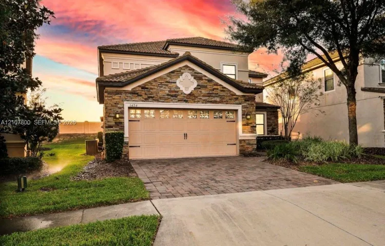 Two-story residence featuring stacked stone veneer, a multi-paneled garage door, decorative gable medallion, tile roofing, and a paved stone driveway