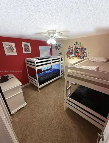 Textured ceiling with a ceiling-mounted light fixture and fan, carpeted flooring, and a single window with horizontal blinds