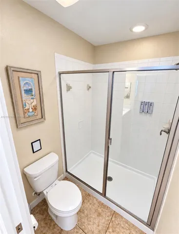 Walk-in shower featuring a white tile surround, glass enclosure, metal framing, and recessed ceiling lighting