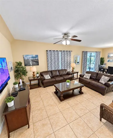 Spacious room featuring vaulted ceilings, neutral wall tones, large-format tile flooring, a central ceiling fan with integrated lighting, and glass sliding doors
