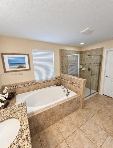 Oval soaking tub with tiled surround, separate glass-enclosed shower, stone-finish countertop, and integrated ceramic sink