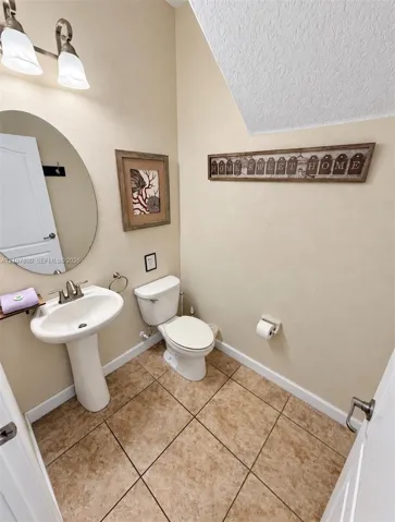 Pedestal sink with chrome faucet, oval wall-mounted mirror, two-light fixture with glass shades, and ceramic tile flooring
