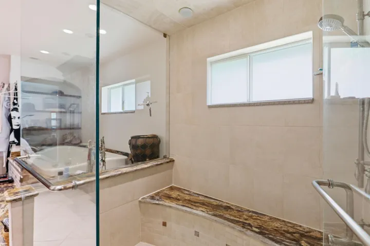 Walk-in shower featuring a glass enclosure, built-in stone bench, integrated rain shower head, and neutral large-format wall tile