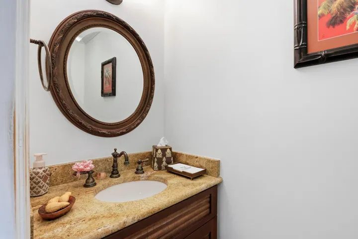 Vanity featuring a stone countertop with an integrated oval sink, dark wood-finish cabinetry, ornate round wall mirror, and dual-handle bronze faucet