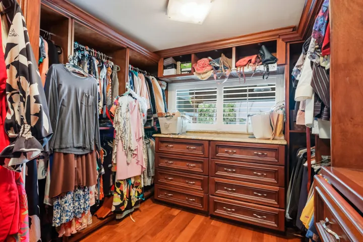 Custom walk-in closet featuring extensive dark wood cabinetry, integrated drawer storage, overhead shelving, plantation shutters, and polished wood-finish flooring