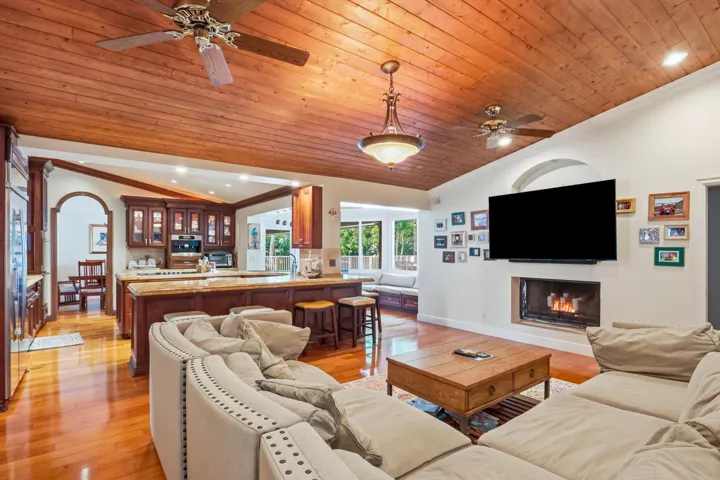Vaulted ceiling with wood-plank finish, integrated ceiling fans, recessed lighting, and central pendant fixture