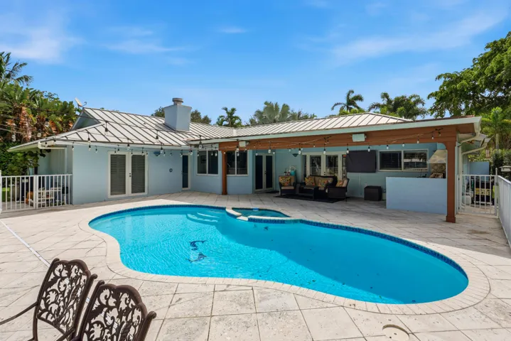 Outdoor living area featuring a covered lanai, built-in masonry grill, custom-shaped swimming pool with integrated spa, and expansive stone-paver decking