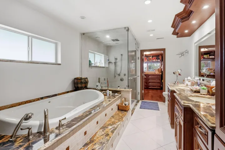 Bathroom featuring a jetted soaking tub with stone surround, custom wood-finish cabinetry, stone countertop, glass-enclosed shower, and tile flooring