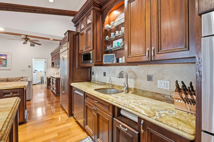 Kitchen featuring custom wood cabinetry, stone countertops, stone tile backsplash, stainless steel appliances, and wood-finish flooring