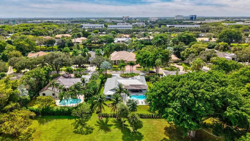 Aerial perspective featuring expansive landscaped grounds, mature canopy trees, multiple in-ground swimming pools, and residential structures with pitched roofing