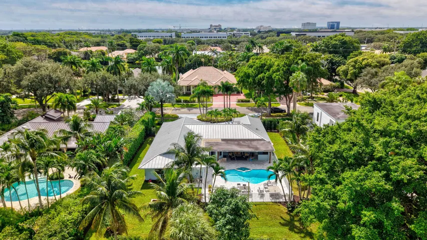 Aerial perspective featuring a single-story residence with a metal roof, an in-ground swimming pool, a stone-paved patio, and mature tropical landscaping