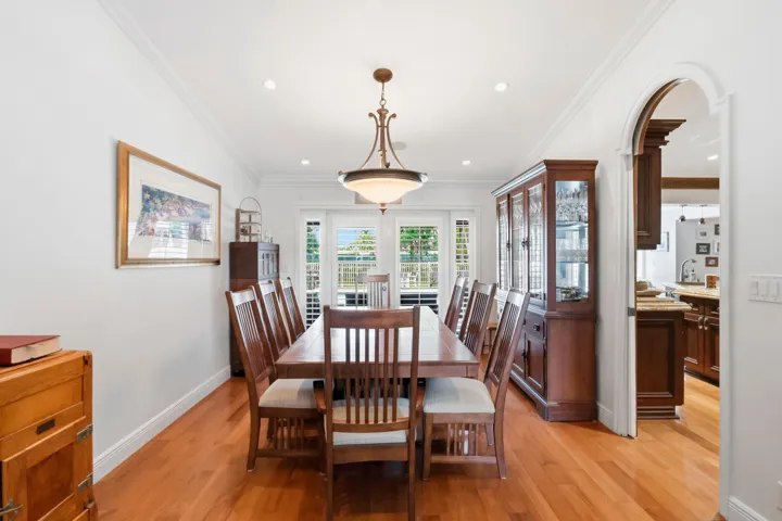 Dining area featuring wood-finish flooring, crown molding, recessed lighting, a central pendant fixture, and an arched doorway