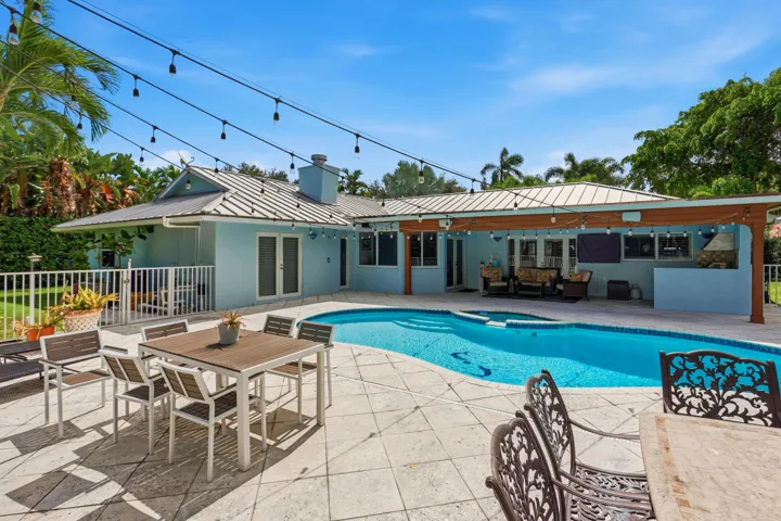Backyard featuring a custom-shaped swimming pool, expansive paved patio, covered outdoor living area, and built-in masonry grill