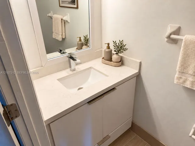 Glossy white vanity featuring a rectangular under-mount sink, light-toned stone countertop, polished chrome single-handle faucet, and hardware-mounted towel bars