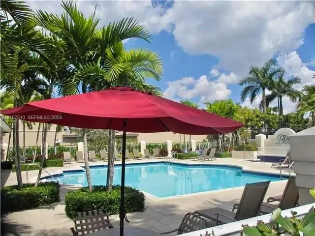 Swimming pool with stone-tiled decking, integrated landscaping featuring palm trees, and perimeter masonry wall