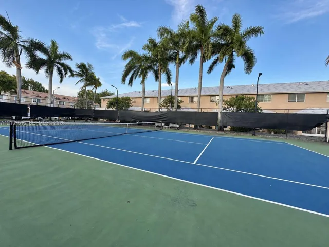 Tennis court featuring a hard surface, perimeter fencing, and established palm trees