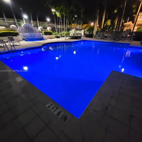 Swimming pool featuring a paved deck, perimeter lighting, and mature palm trees