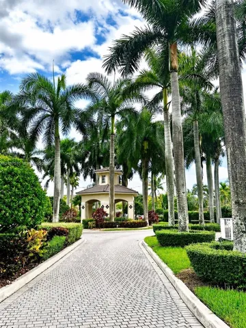 Paver stone driveway leading to a covered pavilion, surrounded by mature palm trees and manicured shrubbery