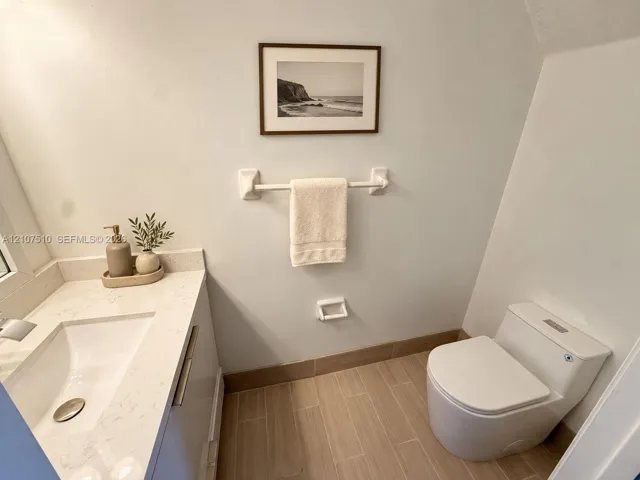 Contemporary vanity with integrated basin and light-toned stone countertop, paired with wood-finish tile flooring and a dual-flush toilet